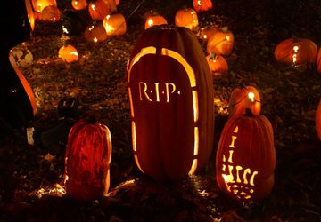 Two pumpkins carved with a skeleton hand pointing up and a tombstone