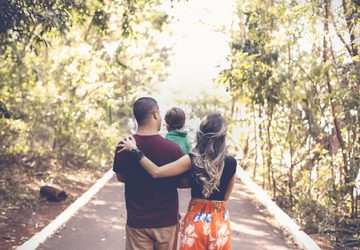 Young family walking in a light forest and carrying their toddler