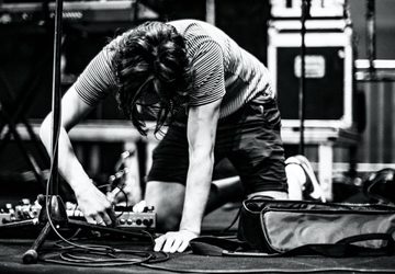 Black and white image of a person plugging in a pedalboard on stage