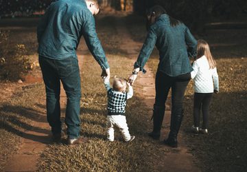 Young family walking a green forest and holding hands with their toddler
