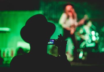 Person recording video of a person playing guitar onstage